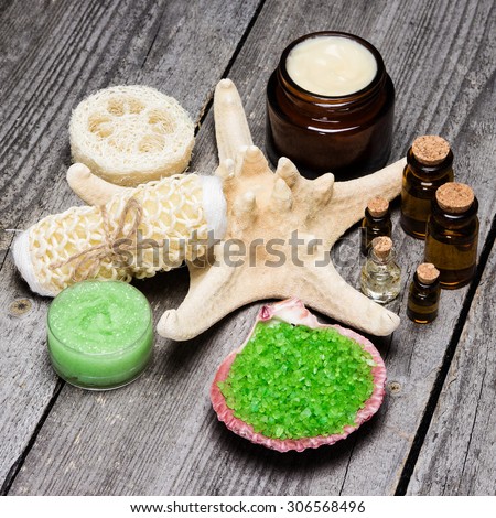 Various spa cosmetics and accessories: sea salt in shell, loofah, skin care cream, natural honey and lemongrass scrub, essential oils with starfish on old wooden planks