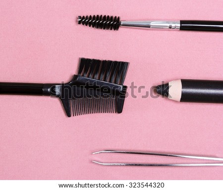 Accessories for care of brows: eyebrow pencil, tweezers, brush and comb on pink colored textured surface. Eyebrow grooming tools