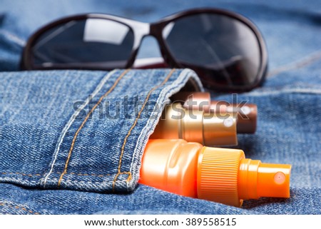 Cosmetic sunscreen products in jeans pocket on the background of sunglasses. Skin care cosmetics containing sun protection factor