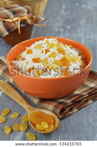 Rice with dried fruit in an orange bowl on wooden table