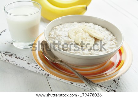 Porridge with bananas in a yellow bowl and a glass of milk on the table