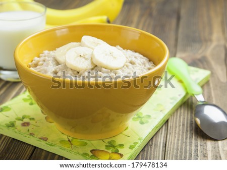 Porridge with bananas in a yellow bowl and a glass of milk on the table