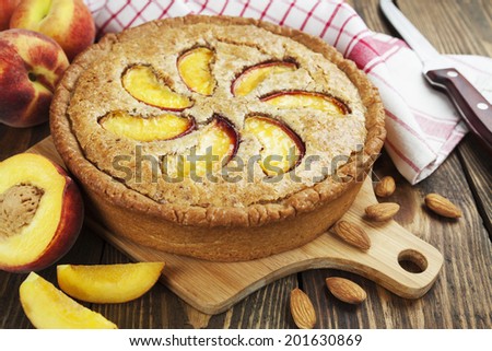 Peach pie with almonds in the ceramic pot on the wooden table