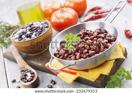 Bean stew in a metal pan and hot chili peppers on a wooden table