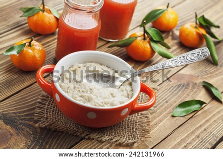 Porridge in an orange bowl, juice and mandarins on the table