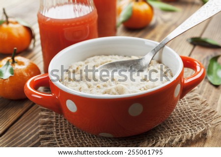 Porridge in an orange bowl, juice and mandarins on the table