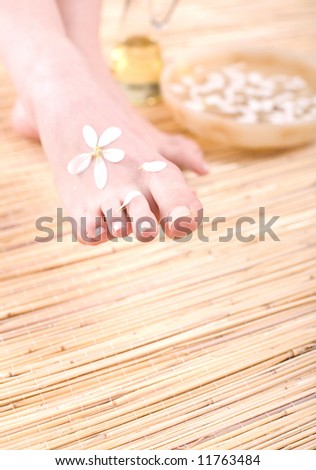 Beautiful female feet with petals on the bamboo mat.