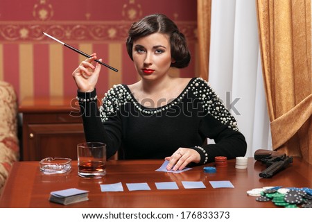 The woman in strict clothes in a retro style. The mafia, plays poker, smokes a cigar or cigarettes and drinks whiskey.