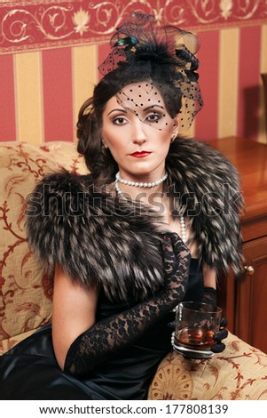The woman in strict clothes in a retro style the tritsatykh of years. The mafia, plays poker, smokes a cigar or cigarettes and drinks whisky.