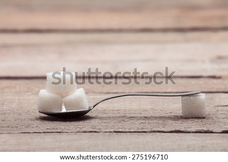 The refined sugar in cubes in a tea spoon on a wooden table from old boards.
