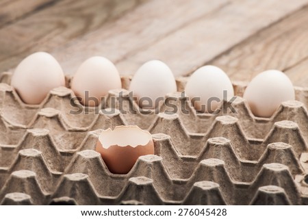 Eggs in a paper tray on a wooden table from boards, with the split egg in the foreground, nobody.