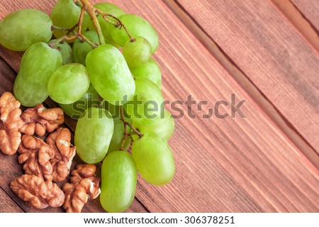White grapes of green color and walnut on a wooden table from boards, macro.