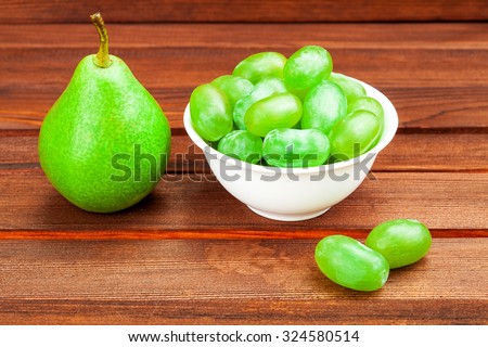Green ripe pear and White grapes in a drinking bowl on a wooden table from boards.