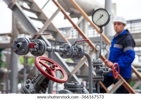The oil refinery, the worker in a difokus checks the indication of a monometer and examines gates and cranes.
