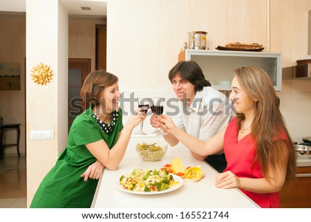 One man and two woman drink red wine on kitchen