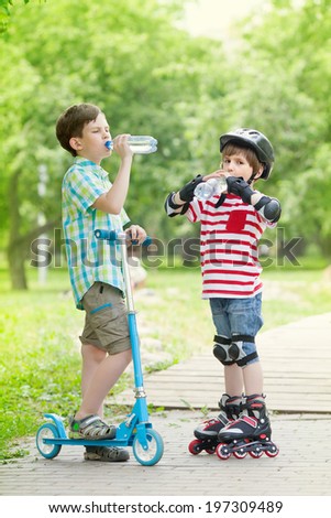children with scooter and rollers drink water, standing on the path in the Park