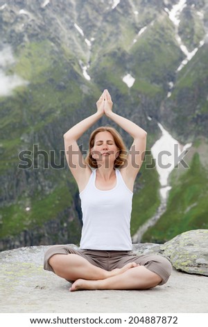 Woman relaxing in yoga position with closed eyes and hand up against mountains