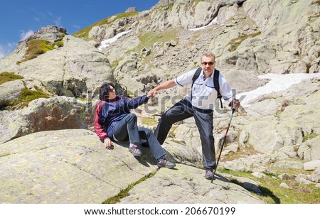 The man helps the woman to get up from a stone in mountains