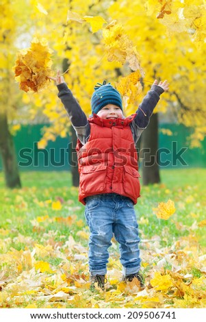 the little boy throws up in the air yellow maple leaves in autumn Park
