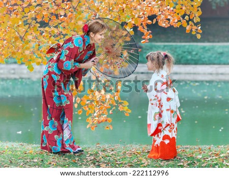 The woman and girl dressed in Japanese kimono walk in autumn park