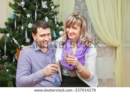 a couple of middle age with glasses of champagne sit at the Christmas tree