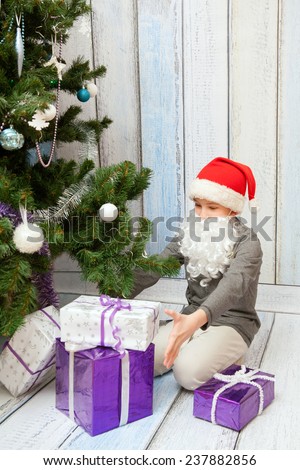The kid is opening New Year presents at the Christmas tree