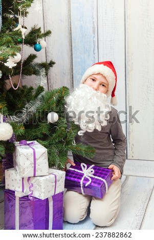 The young Santa Clause sits under the Christmas tree with new year presents