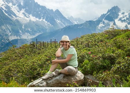 Middle age woman rests on stone in high mountains