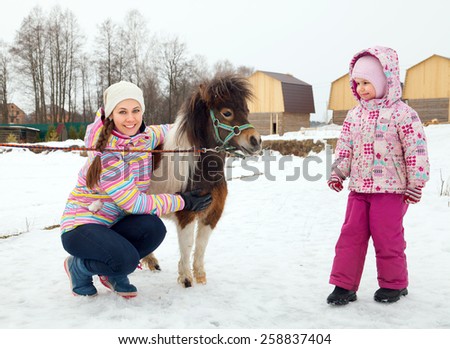 Young woman and girl walk with miniature horse in winter park