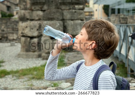 The boy drinks water from plastic bottle during excursion in old city