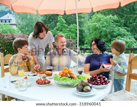 A family from five people are having dinner on a terrace in summer hot day