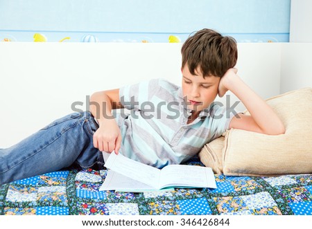 A schoolboy reads the summary of the lesson, lying on the sofa at home