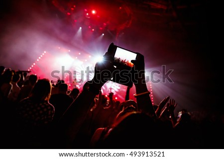 Hand with a smartphone records live music festival, Taking photo of concert stage, live concert, music festival, happy youth, luxury party, landscape exterior - purple light