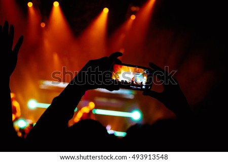 Hand with a smartphone records live music festival, Taking photo of concert stage, live concert, music festival, happy youth, luxury party, landscape exterior - purple light