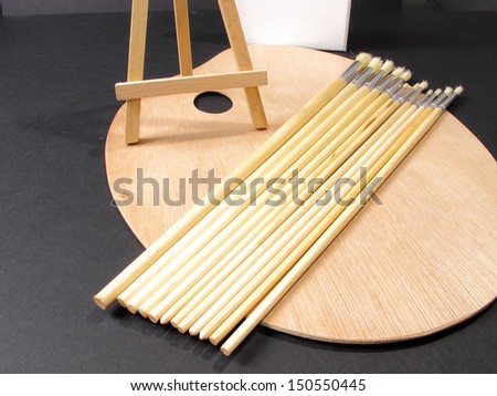 An image of paint brushes and an Easel laying on a painters pallette / Things an Artist uses