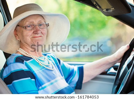 smiling old woman in glasses driving automobile