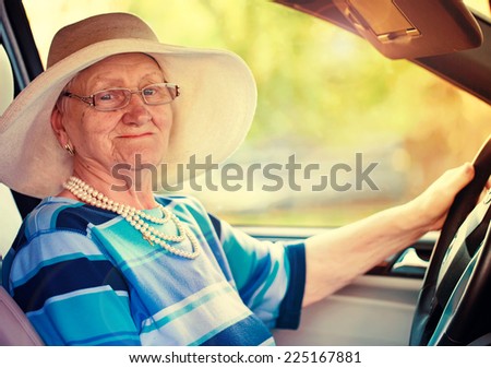 smiling old woman in glasses driving automobile