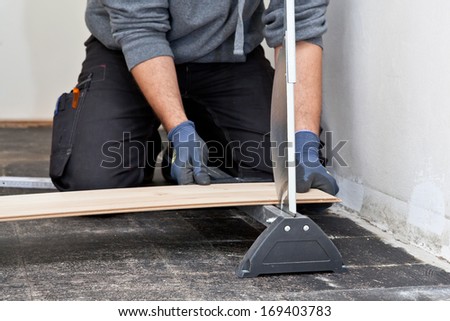 Carpenter or builder measuring and cutting a new wooden floor board for installation during renovation or construction of a building