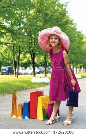 Enthusiastic girl standing on the street with shopping bags in elegant hat and her mother\'s shoes