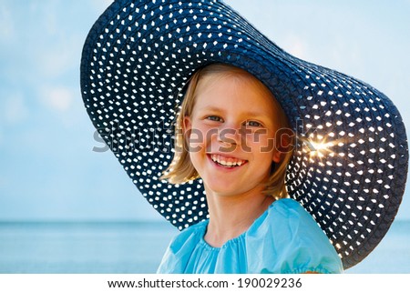 smiling girl in a blue hat and turquoise dress standing on background of ocean
