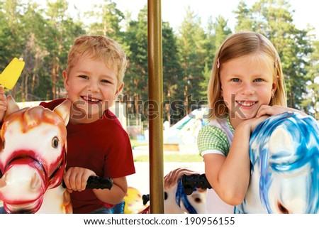 brother and sister ride the carousel in an amusement park in the summer