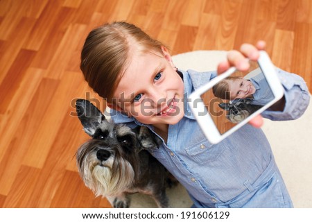 Little girl taking photo of herself and her dog with mobile phone camera