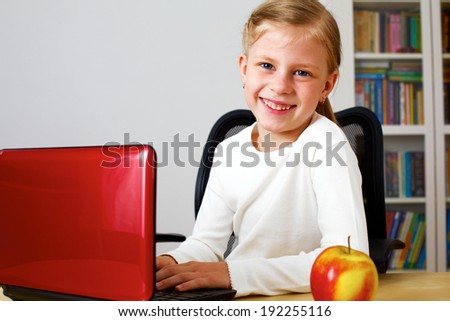 Schoolgirl working on a laptop while sitting at table at home