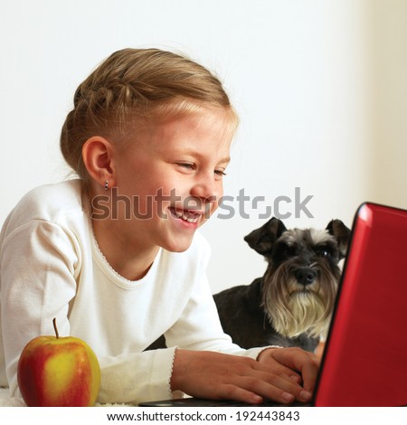 Schoolgirl studies at home on a laptop next to her is her dog
