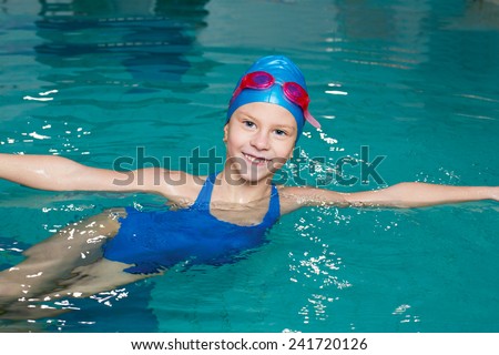 beautiful girl in a bathing suit, swim cap, goggles, holding on overboard in a swimming pool