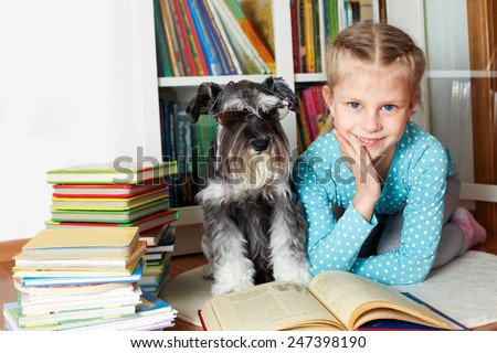 girl and her dog in glasses reading a book, sitting on floor in library