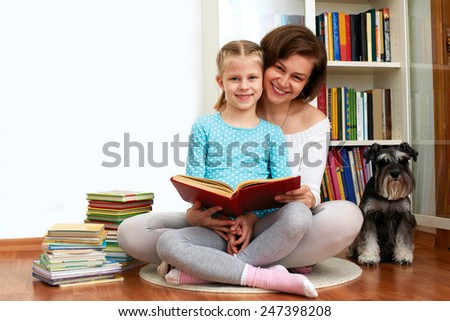Mom reading a book her little daughter. beside them sitting dog