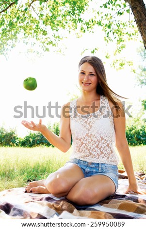 young girl throws up an apple. beautiful girl has a rest in the summer in the park.