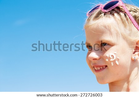 Suntan lotion girl applying sunscreen solar stream. Beautiful happy cute girl applying suntan cream on her face over ocean background. Sun tanning. Skin care and protection. Vacation