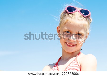 Suntan lotion girl applying sunscreen solar stream. Beautiful happy cute girl applying suntan cream on her face over ocean background. Sun tanning. Skin care and protection.